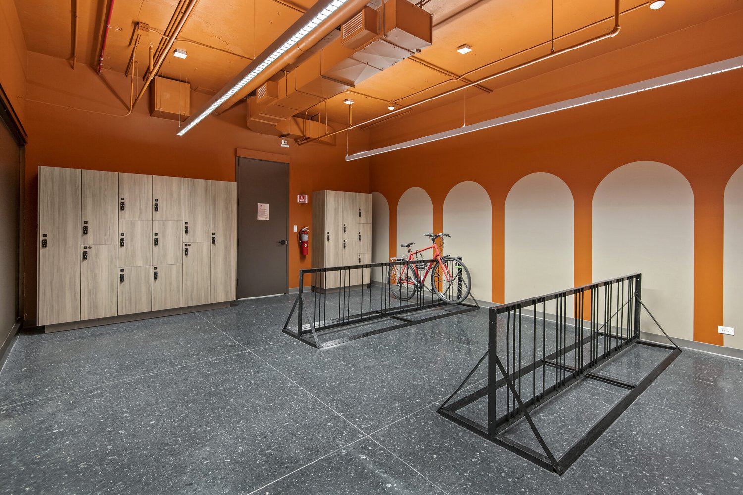 Secure bike room with bike racks, wood-finish lockers and bold orange arched walls