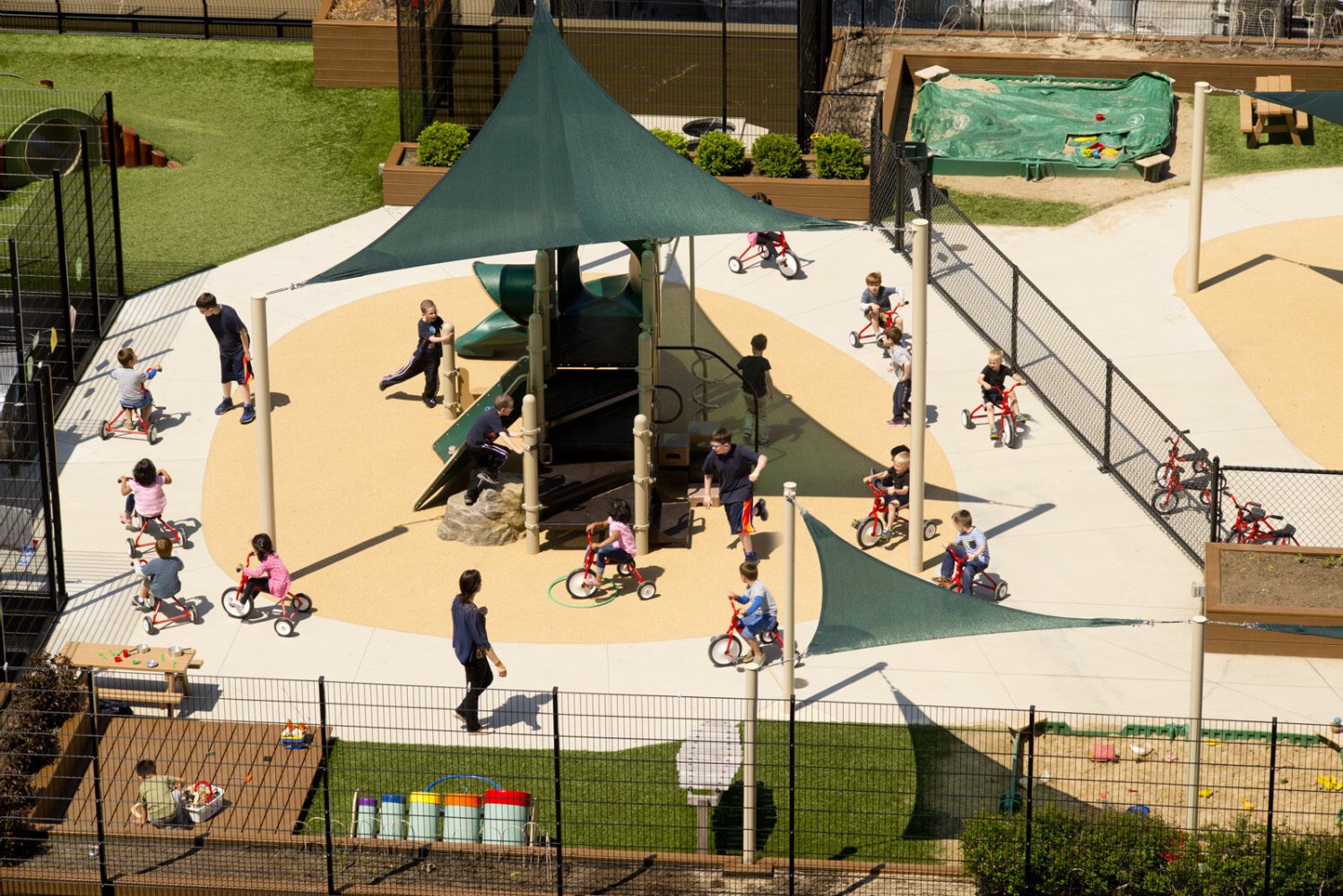 Children riding tricycles around a shaded play structure at the Bright Horizons daycare outdoor play area