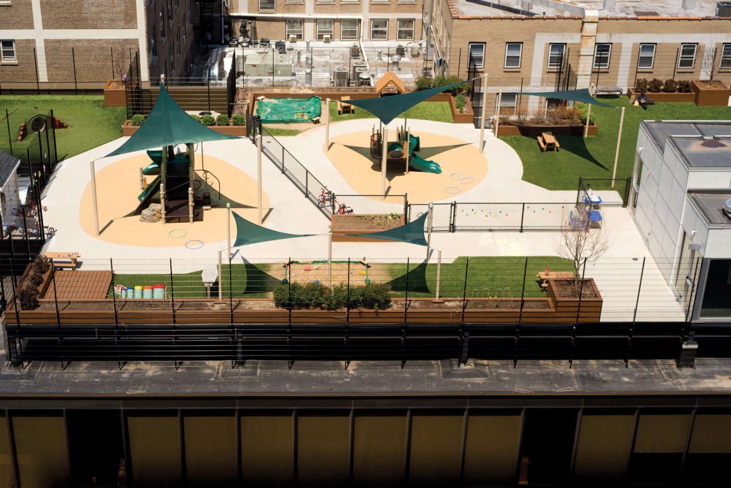 Bright Horizons rooftop play area with green shade sails, slides, lawn and planters